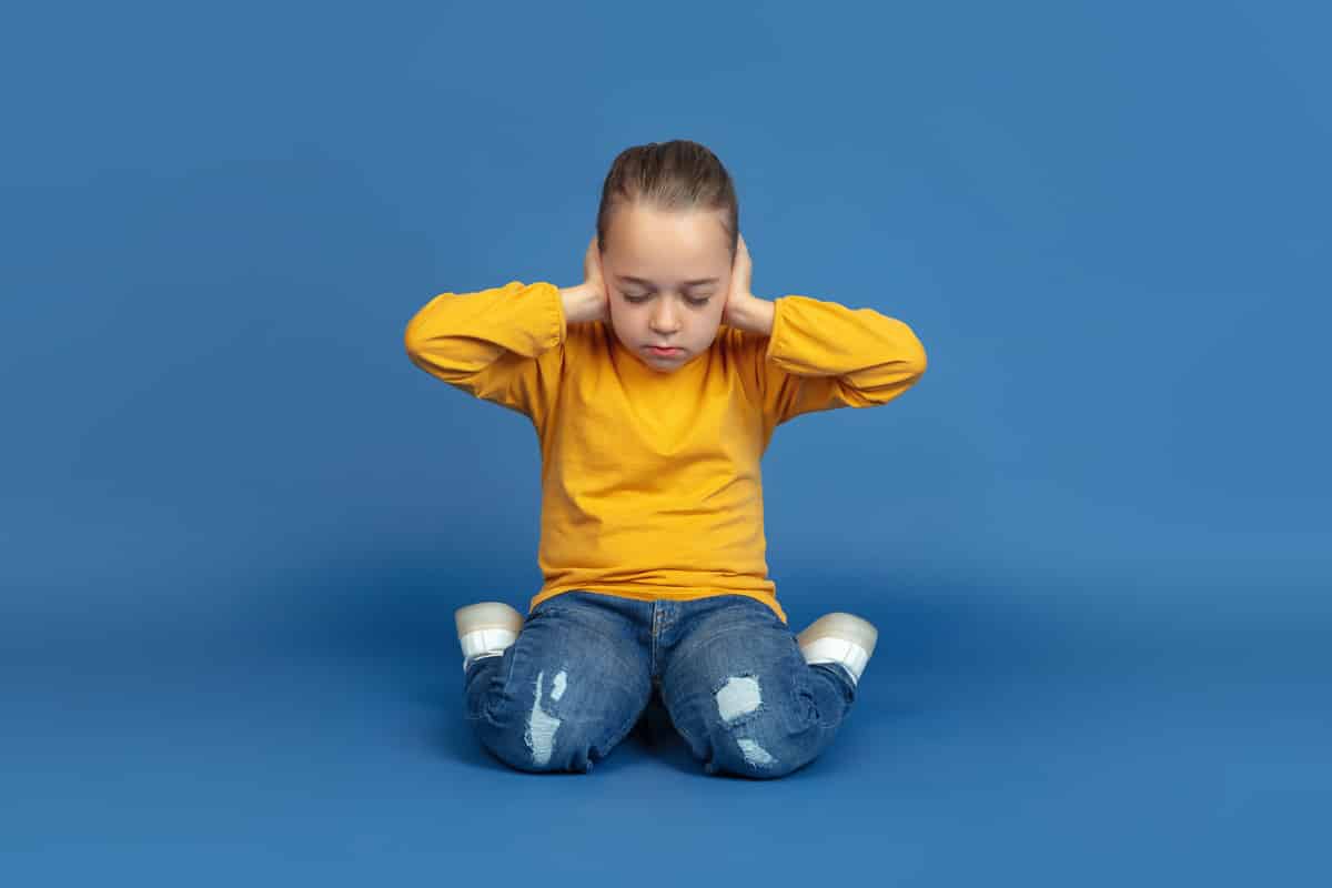 Niño sentado, tapandose los oídos